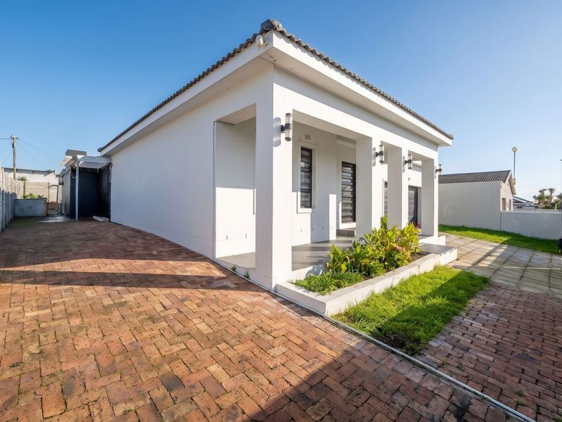 Front elevation of a modern house featuring a brick paved driveway, covered entrance porch with concrete pillars, and a well-maintained garden bed.