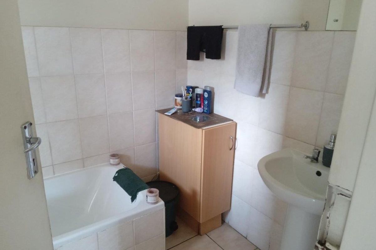A functional bathroom featuring a tiled bathtub, pedestal basin, and built-in vanity cabinet with neutral wall tiling.