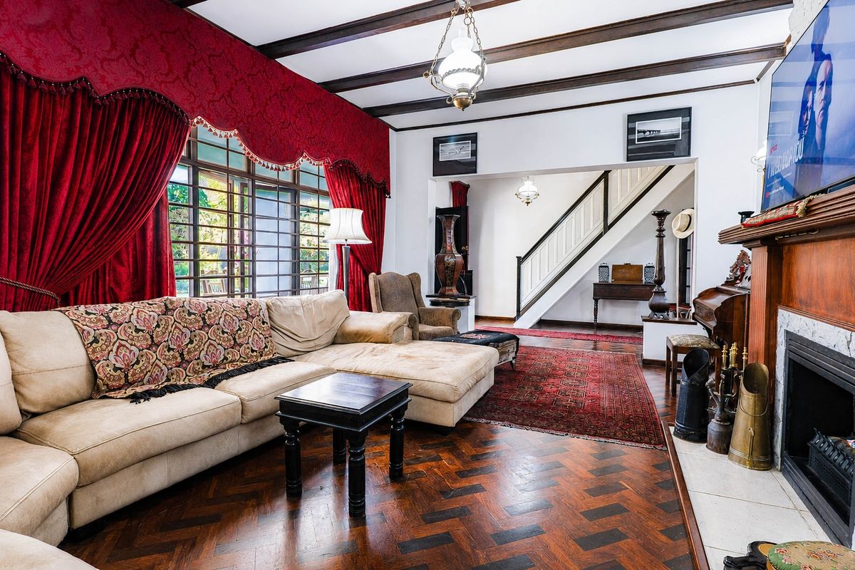 Spacious living room featuring classic herringbone parquet flooring, exposed timber ceiling beams, and a traditional fireplace with a marble hearth and timber mantelpiece.
