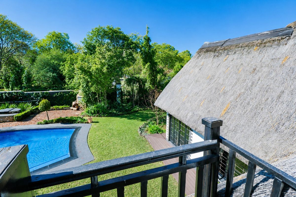 Elevated view of a rear garden featuring a swimming pool, paved patio area, and a thatched roof structure with a balcony.