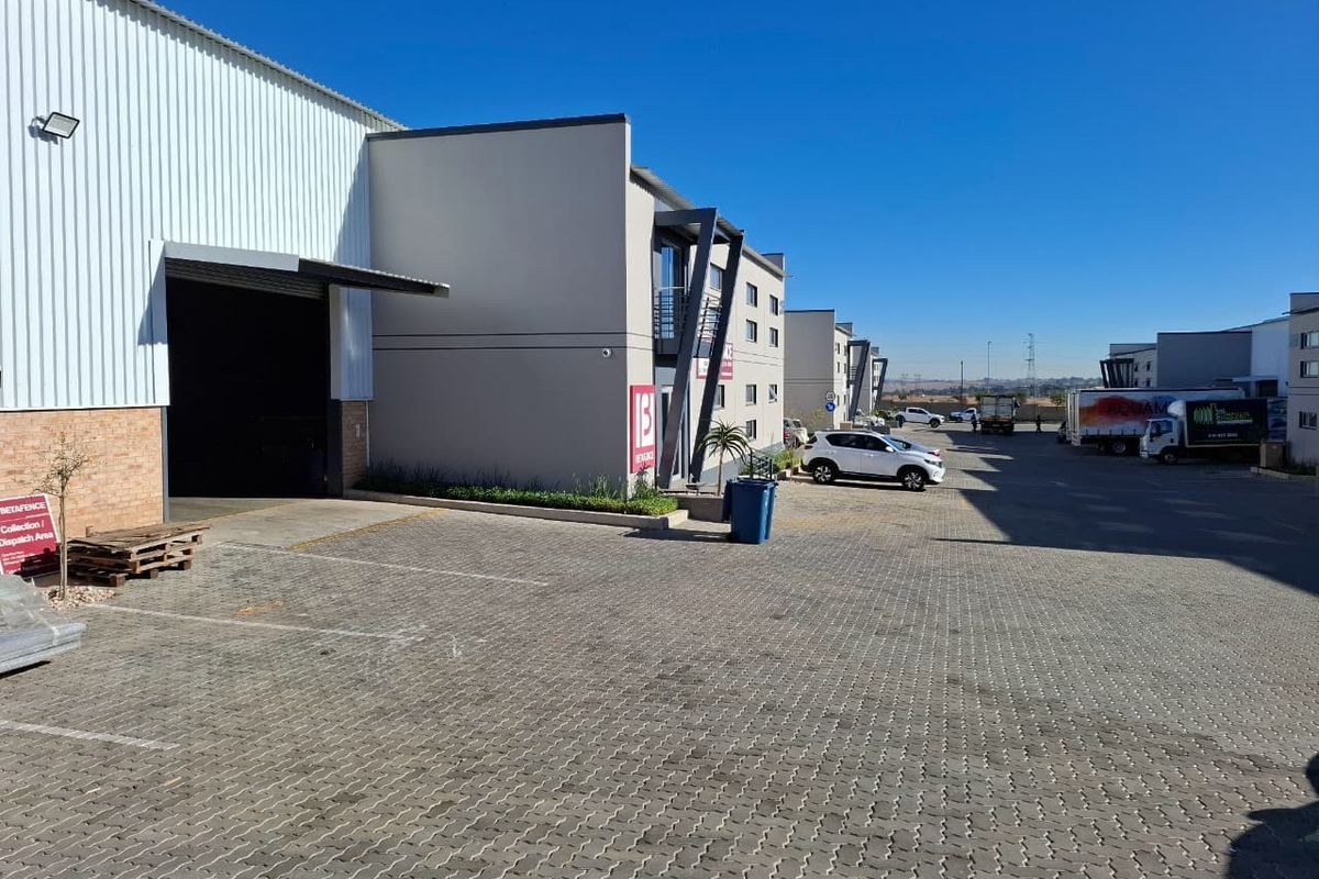 Exterior view of an industrial warehouse facility featuring a paved loading yard, roller shutter door access, and modern office facade components.
