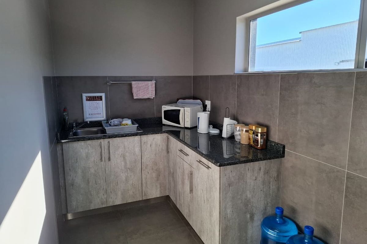 A compact industrial kitchenette featuring modern grey cabinetry, granite countertops, a stainless steel sink, and tiled splashbacks.