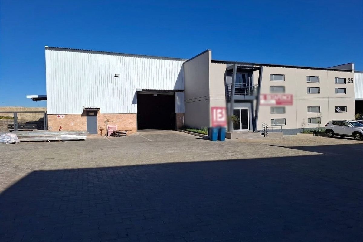 Industrial warehouse facility featuring a large roller shutter door, paved yard area, and integrated office space with a balcony.