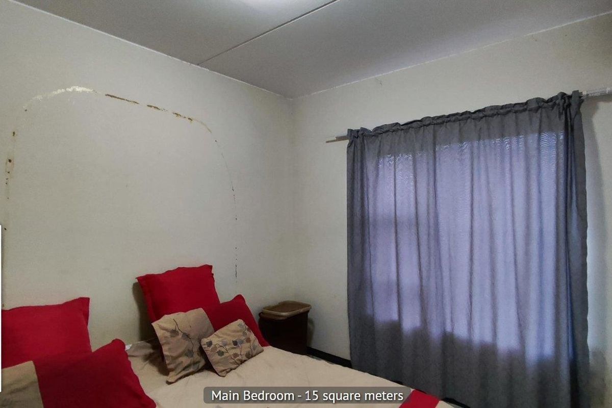 A bedroom featuring a window with curtain rail and visible wall surface damage requiring repair.