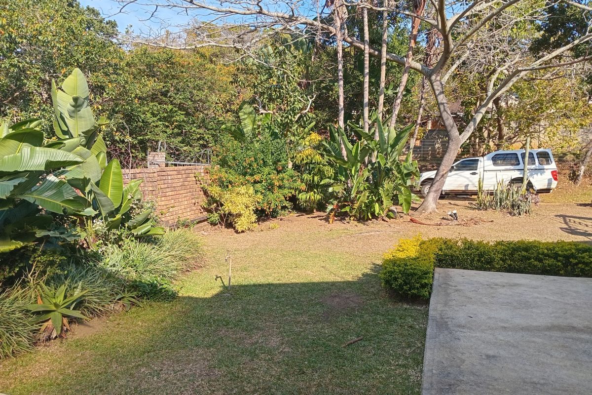 A private rear garden featuring a lawn, established trees, mature shrubs, and a concrete patio area enclosed by a brick boundary wall.