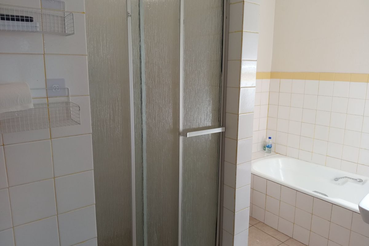A functional bathroom featuring a built-in bathtub and a separate shower enclosure with tiled walls and flooring.