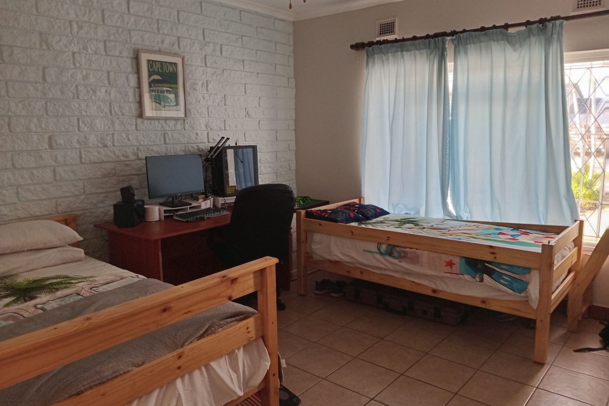 A bedroom featuring a painted brick feature wall, tiled flooring, and large windows with curtain fixtures.