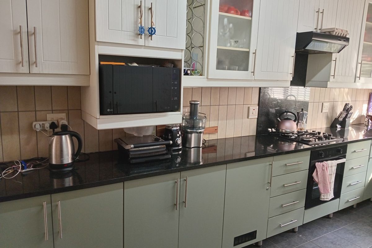 A functional kitchen featuring two-tone cabinetry, black granite countertops, a built-in gas hob, and an integrated oven with an extractor fan.