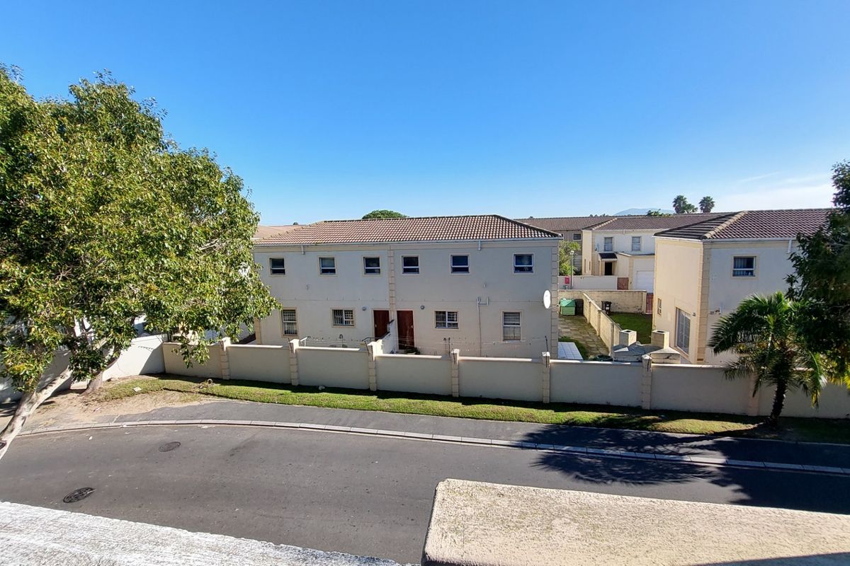 An elevated view of the apartment complex exterior, featuring tiled roofing, perimeter boundary walls, and paved street access.