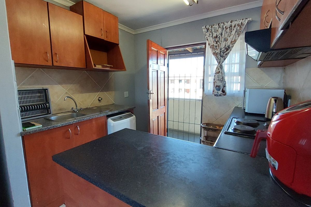 Functional kitchen featuring wooden cabinetry, dark countertops, a built-in hob, and direct access to an outdoor balcony area.