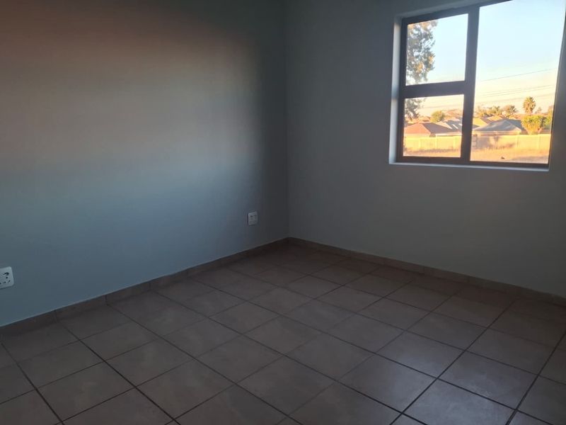 A simple, empty bedroom featuring neutral tiled flooring and a window providing natural light.