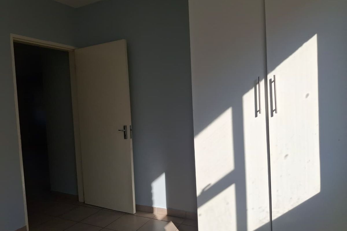 A bedroom featuring built-in cupboards and tiled flooring, illuminated by natural light.