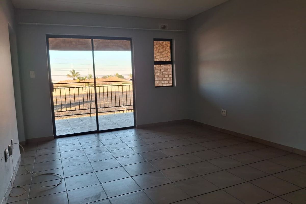 A spacious, tiled living area featuring large sliding glass doors that open onto a private balcony, providing natural light and outdoor access.