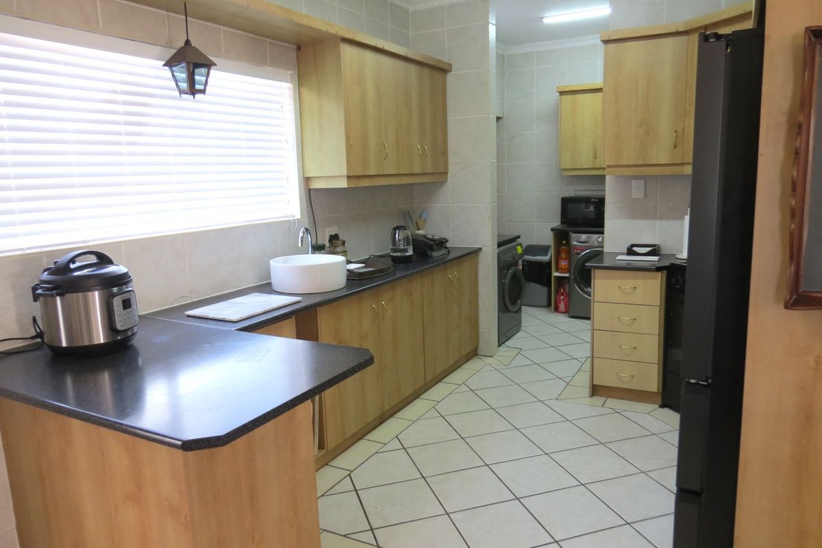 A functional kitchen featuring light wood cabinetry, dark countertops, a basin sink, and an adjoining scullery area with tiled flooring throughout.