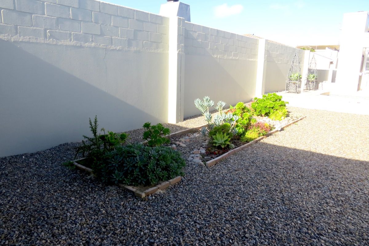 A low-maintenance rear garden area featuring gravel landscaping, raised brick-edged garden beds with succulents, and a high perimeter boundary wall.