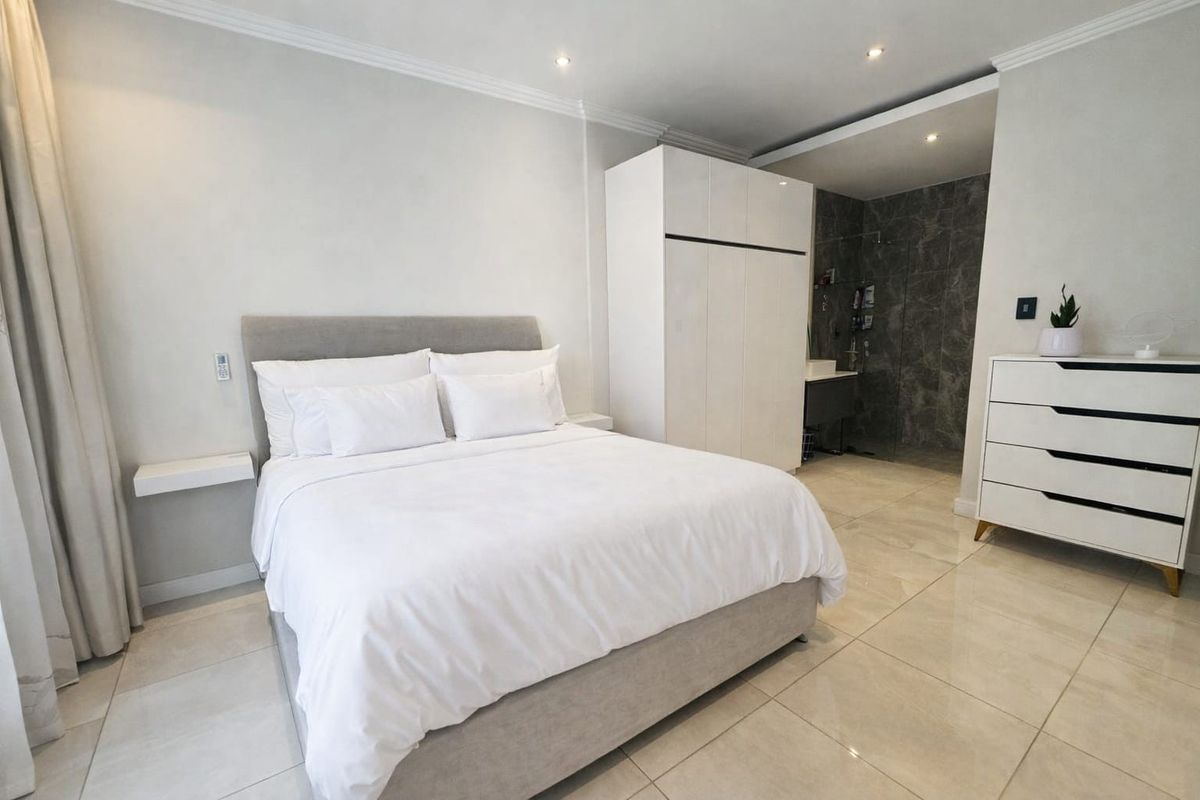 Modern bedroom featuring tiled flooring, recessed ceiling lighting, and an integrated en-suite bathroom with a glass-enclosed shower and stone-look wall tiling.