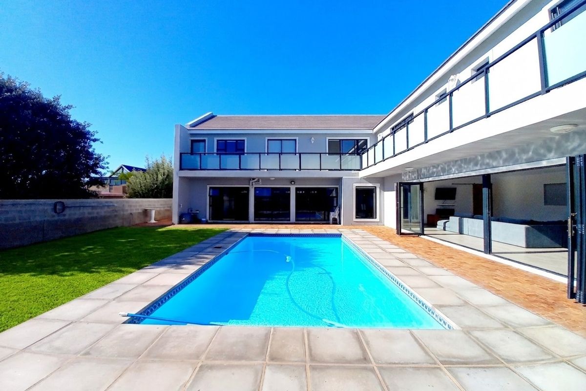 Rear view of a modern two-story house featuring a swimming pool, paved patio area, and a spacious balcony overlooking the garden.