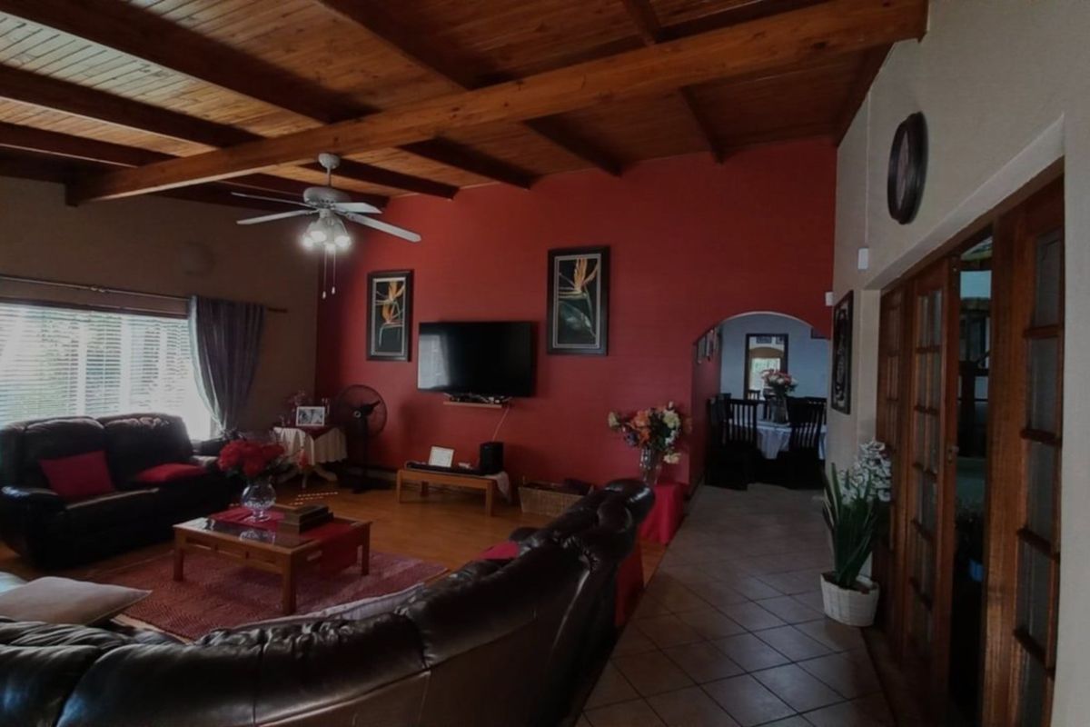 Spacious living room featuring exposed timber beam ceilings, tiled flooring, and an arched entryway leading to the dining area.