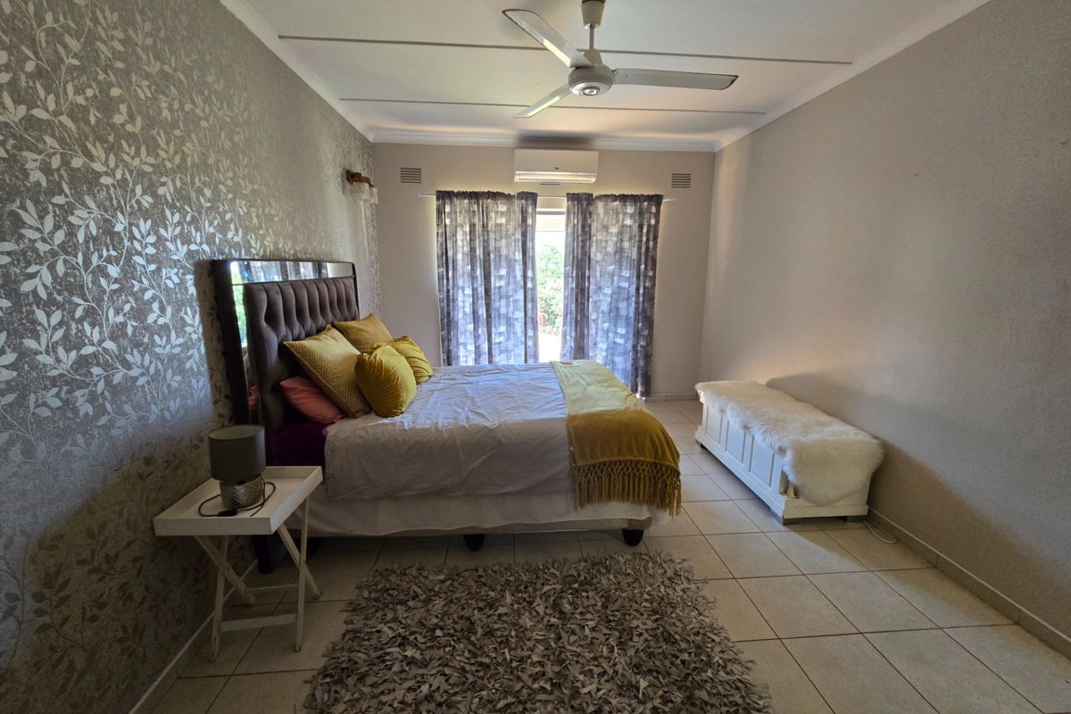 A spacious bedroom featuring tiled flooring, a ceiling fan, and a wall-mounted air conditioning unit.