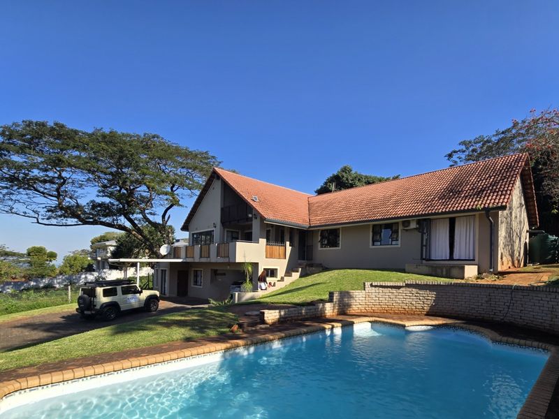 A spacious rear exterior view featuring a swimming pool, landscaped lawn, and a multi-level house with a tiled roof and balcony.
