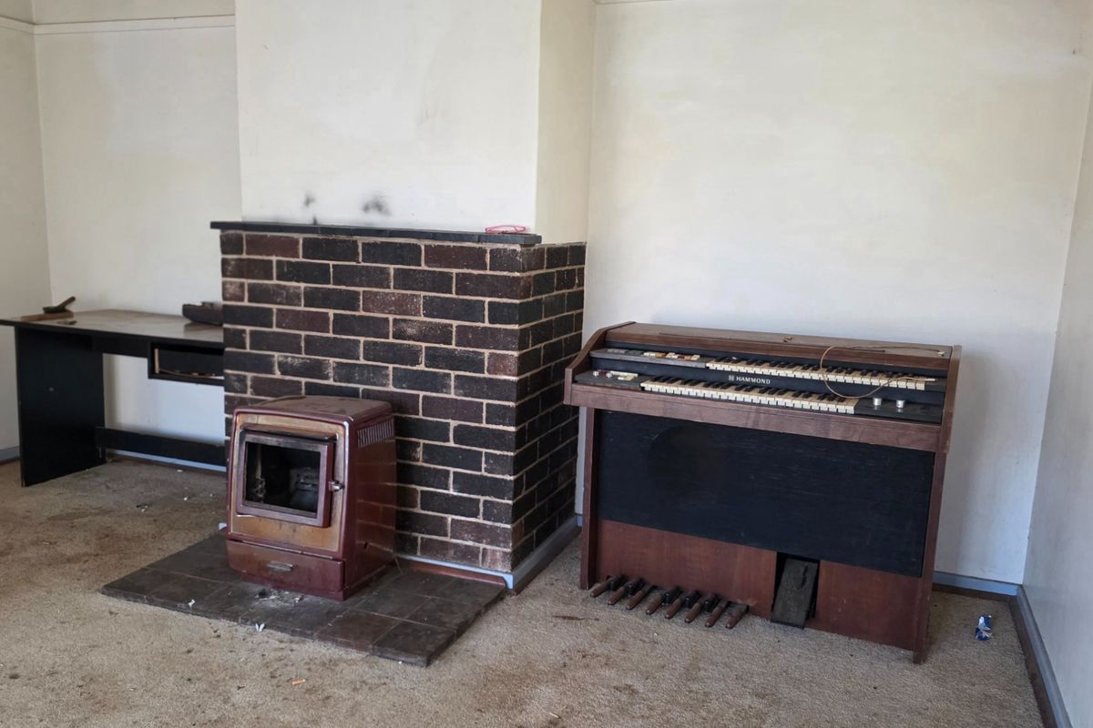 Living room featuring a brick fireplace with a freestanding wood burning stove and tiled hearth, requiring cosmetic updates to the flooring and walls.