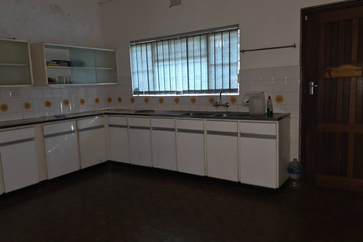 A dated kitchen featuring white laminate cabinetry, a double bowl sink, and tiled splashbacks, requiring cosmetic updates to modernize the space.