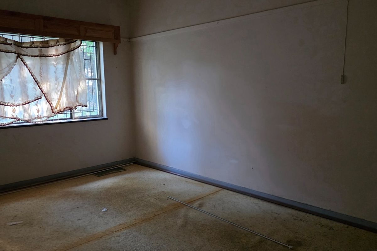 An empty bedroom featuring worn carpeting, security bars on the window, and a timber pelmet, requiring cosmetic updates to restore its appeal.