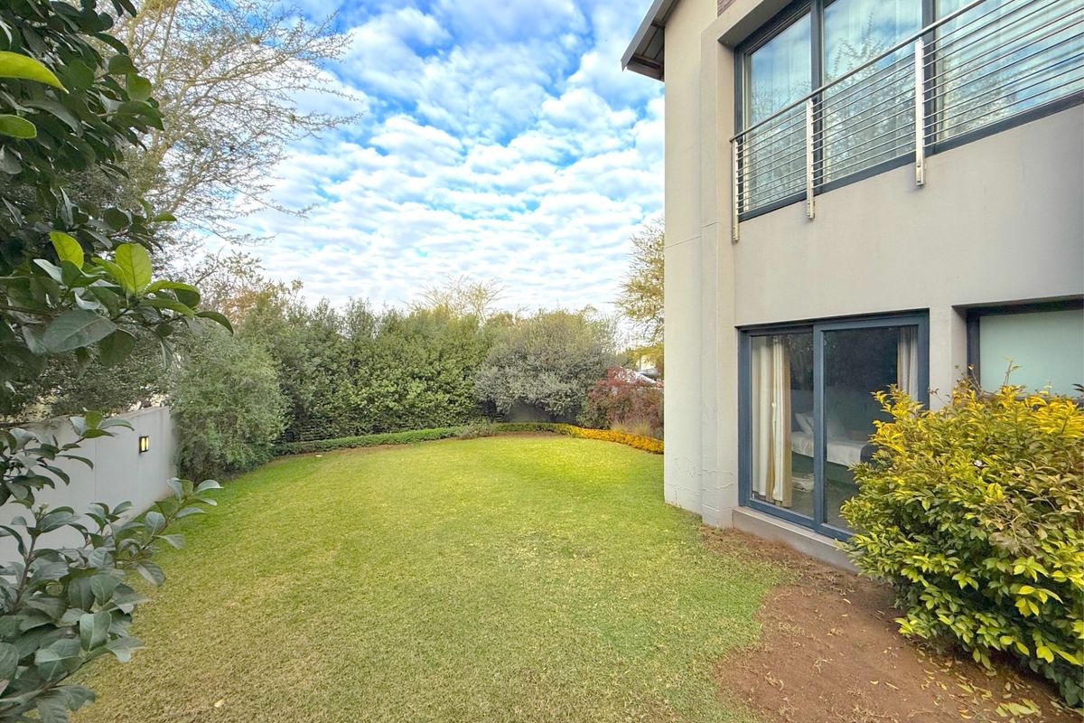 A well-maintained rear garden featuring a manicured lawn, mature perimeter hedging, and a modern two-story building facade with sliding doors and a balcony.