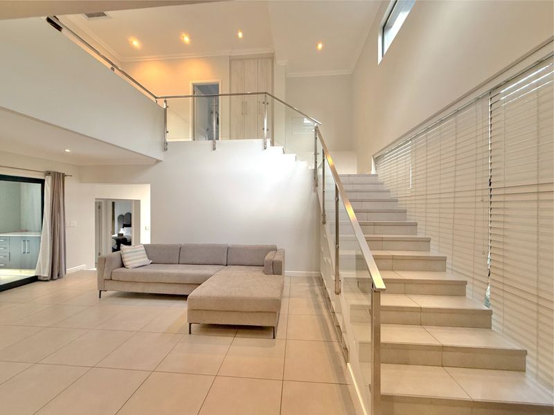 Spacious open-plan living area featuring modern tiled flooring, a striking glass staircase balustrade, and abundant natural light through large windows.