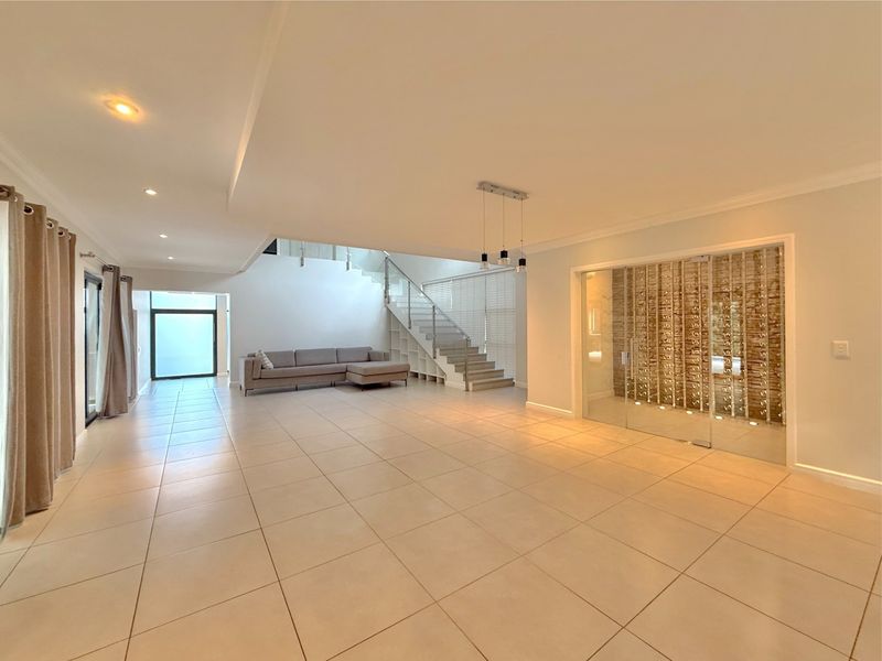 Spacious open-plan living area featuring large format floor tiles, a modern staircase with glass balustrade, and a dedicated glass-enclosed wine cellar.