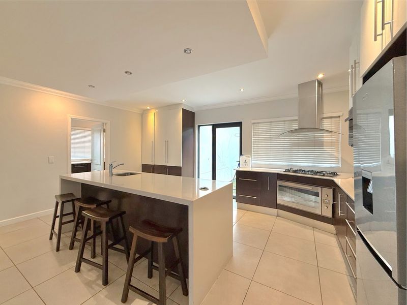Modern kitchen featuring a large central island, built-in oven, gas hob, extractor fan, and sleek cabinetry with neutral tiled flooring.