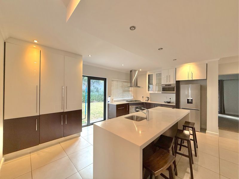 Modern kitchen featuring a central island with stone countertops, ample built-in cabinetry, stainless steel appliances, and direct access to the rear garden.