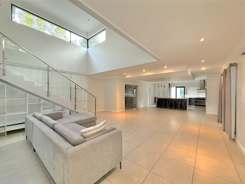 Spacious open-plan living area featuring a modern kitchen with island, high ceilings with clerestory windows, and a contemporary staircase with glass balustrade.