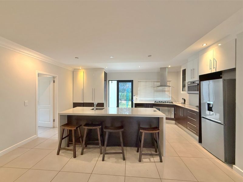 Modern kitchen featuring a central island with stone countertops, dark and white cabinetry, built-in appliances, and tiled flooring with recessed lighting.
