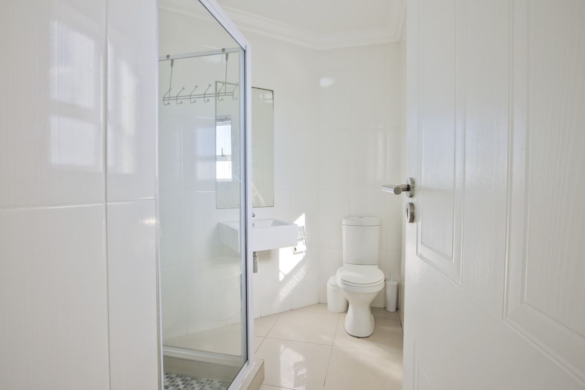 A clean, compact bathroom featuring a glass-enclosed shower, wall-mounted basin, and toilet with white tiled walls and flooring.
