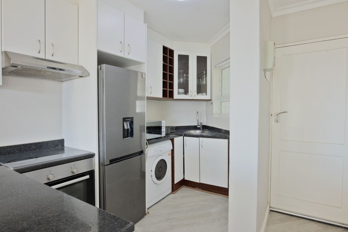 Compact kitchen featuring white cabinetry, dark granite countertops, built-in oven, extractor fan, and integrated space for laundry appliances.