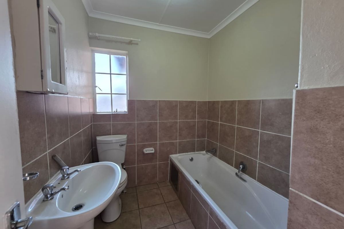 A functional bathroom featuring a pedestal basin, a standard bathtub with tiled surround, and a window for natural ventilation.