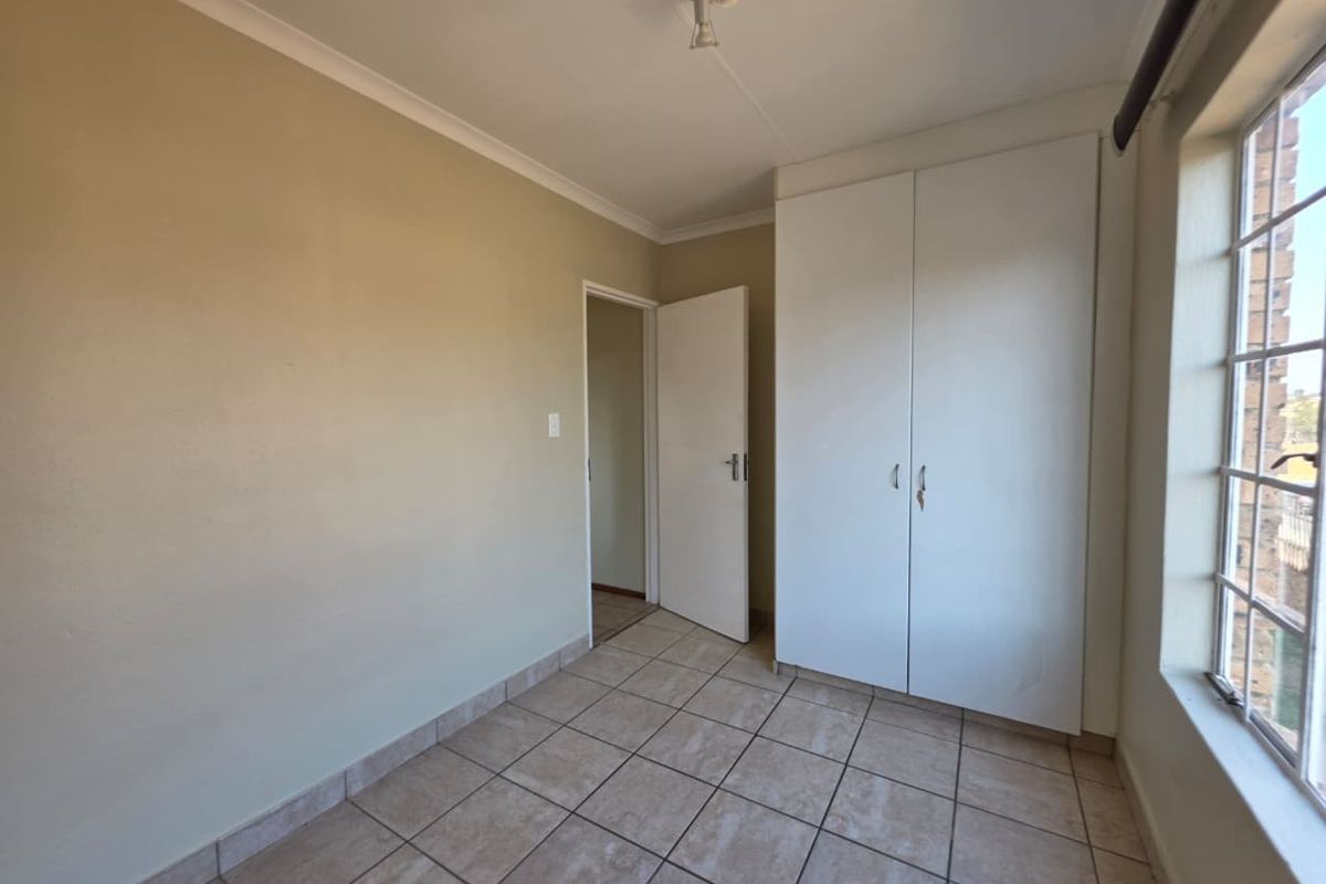A bright, empty bedroom featuring neutral tiled flooring, built-in white cabinetry, and a large window allowing for natural light.