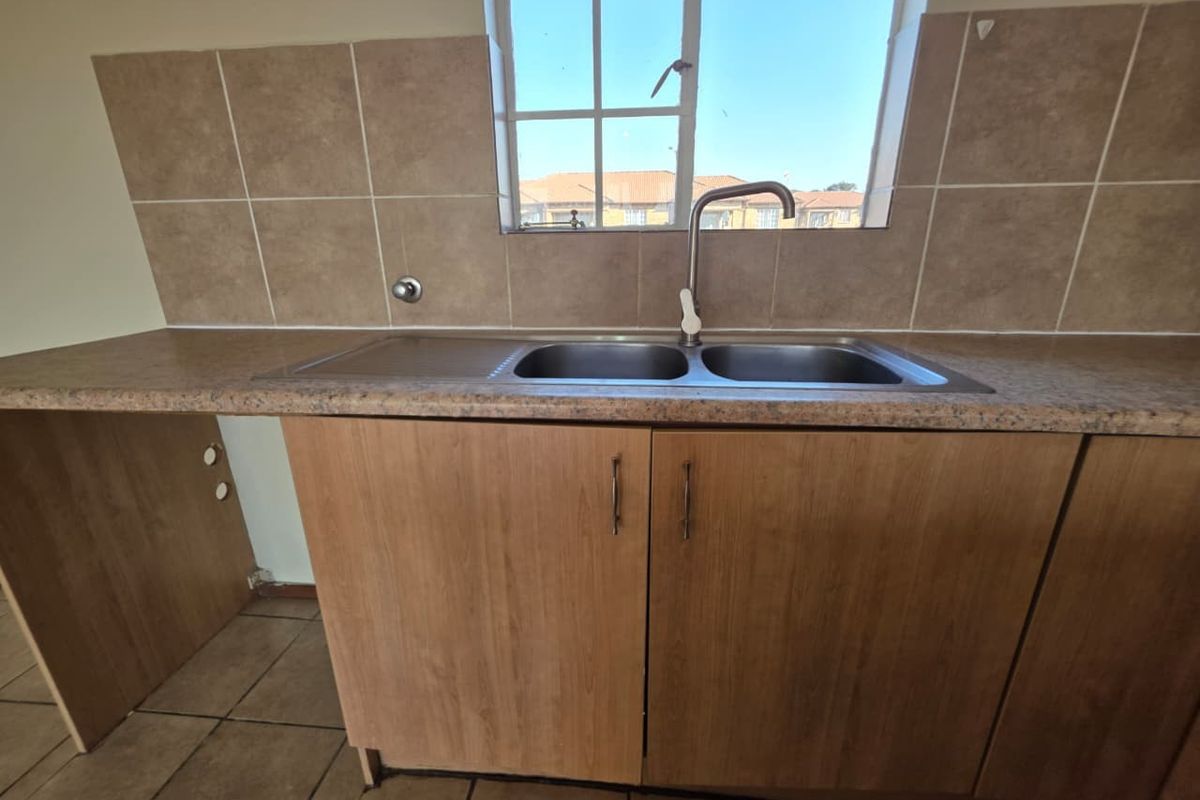 A functional kitchen area featuring wood-look cabinetry, a stainless steel double sink, and tiled splashbacks under a window.