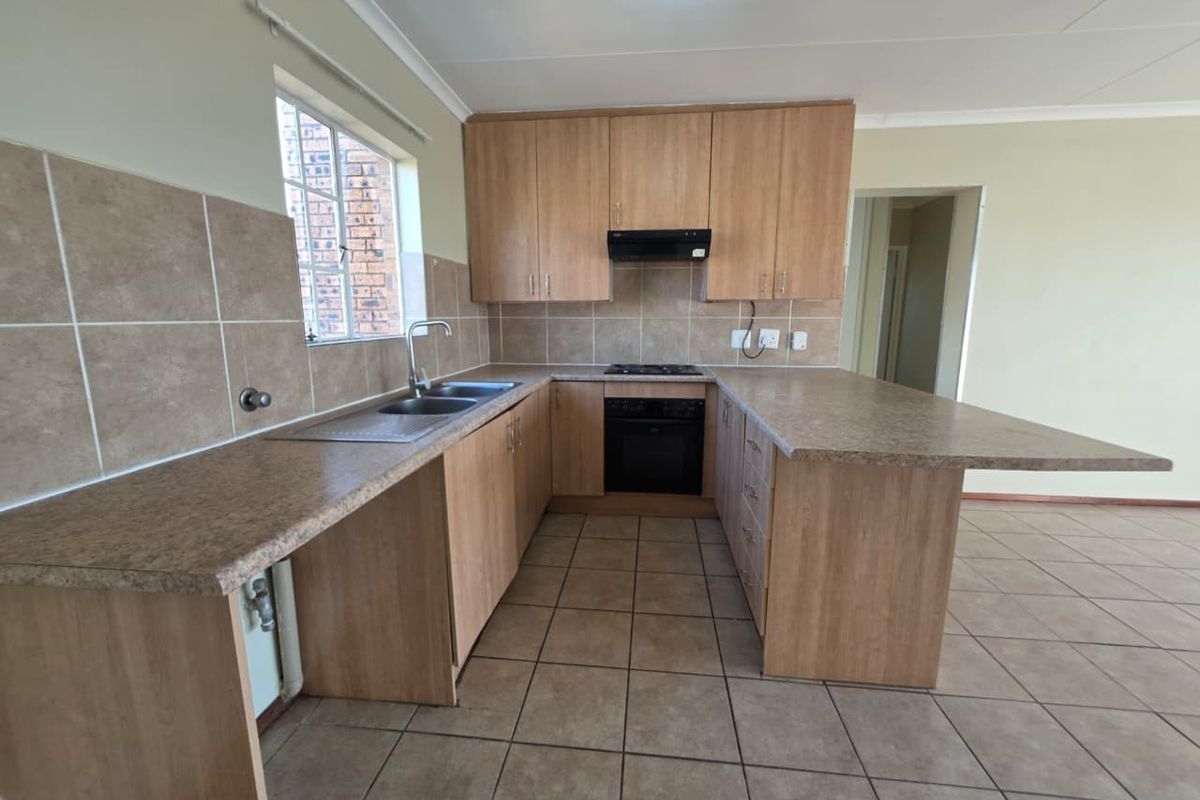 A functional open-plan kitchen featuring light wood cabinetry, a built-in oven, hob, extractor fan, and a breakfast bar counter.