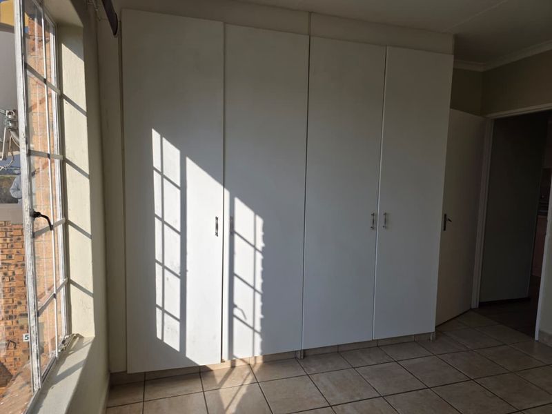 A bedroom featuring built-in white cupboards, tiled flooring, and a large window allowing natural light.