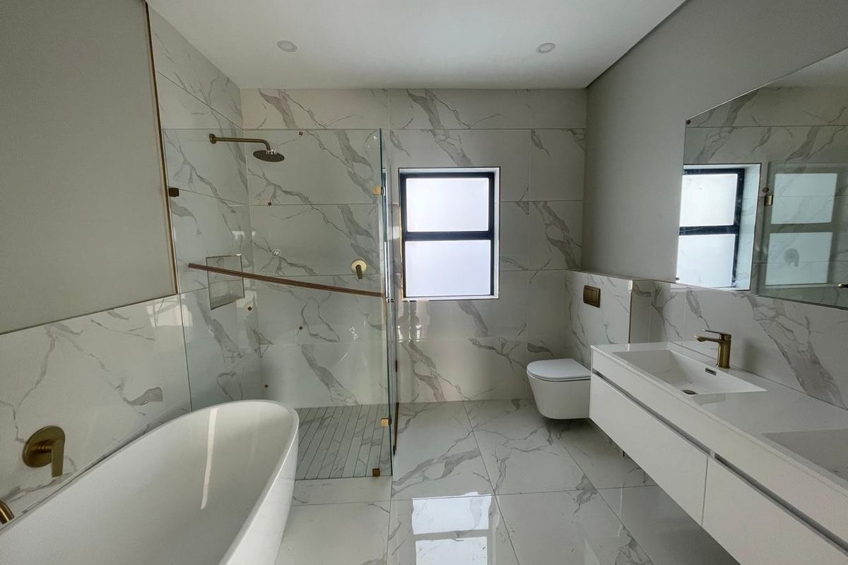 Modern bathroom featuring a freestanding bathtub, glass-enclosed walk-in shower, wall-mounted toilet, and a sleek vanity with marble-look tiling throughout.