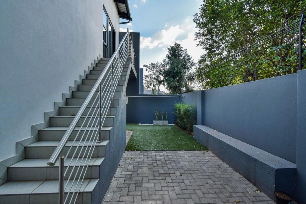 A private rear courtyard featuring paved flooring, a small artificial lawn, and an external staircase with stainless steel railings leading to the upper level.