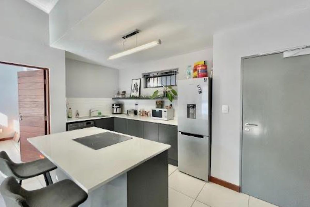 Modern kitchen featuring a central island with an integrated induction hob, sleek dark cabinetry, stone countertops, and tiled flooring.