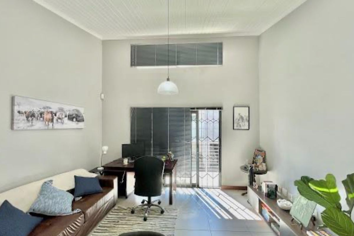 A bright living room featuring high ceilings, tiled flooring, and a sliding glass door with security gate leading to an outdoor area.