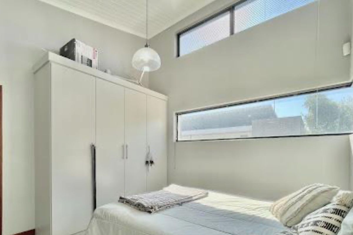 A bright bedroom featuring high ceilings, clerestory windows for natural light, and built-in white cabinetry providing ample storage space.