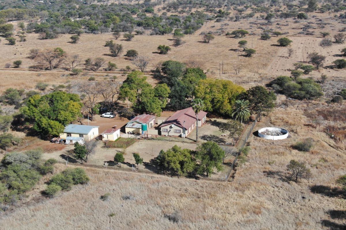 Aerial view of a small holding property featuring a main dwelling, multiple outbuildings, a water reservoir, and fenced grounds in a rural landscape.