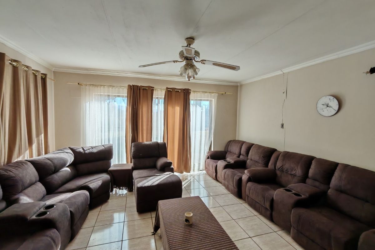 A living room featuring tiled flooring, a ceiling fan, and sliding glass doors leading to the exterior, with a visible wall crack present.