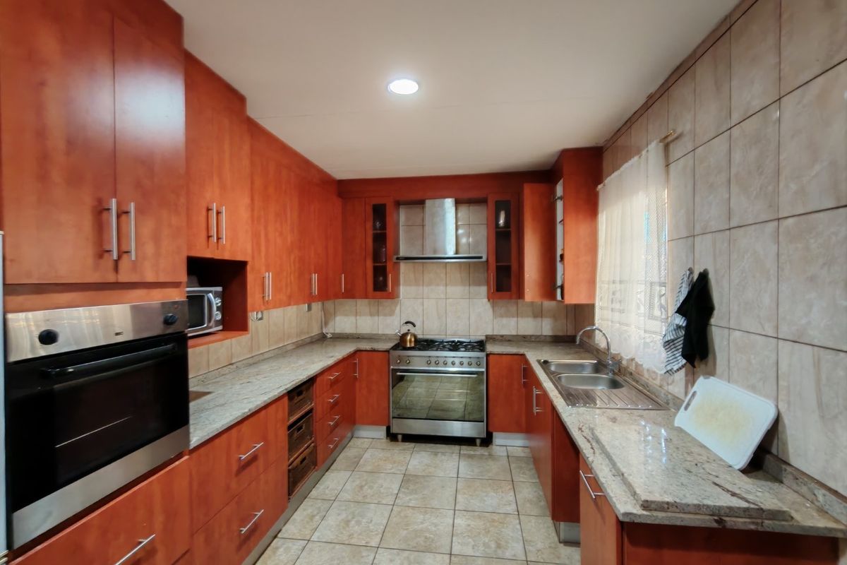A functional kitchen featuring warm-toned wooden cabinetry, granite countertops, a gas hob with extractor, and a double sink with tiled finishes.