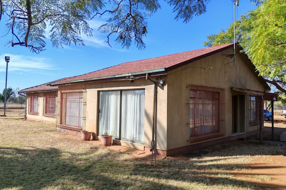 Rear view of a single-story dwelling featuring plastered walls, a tiled roof, and security bars on windows and sliding doors.